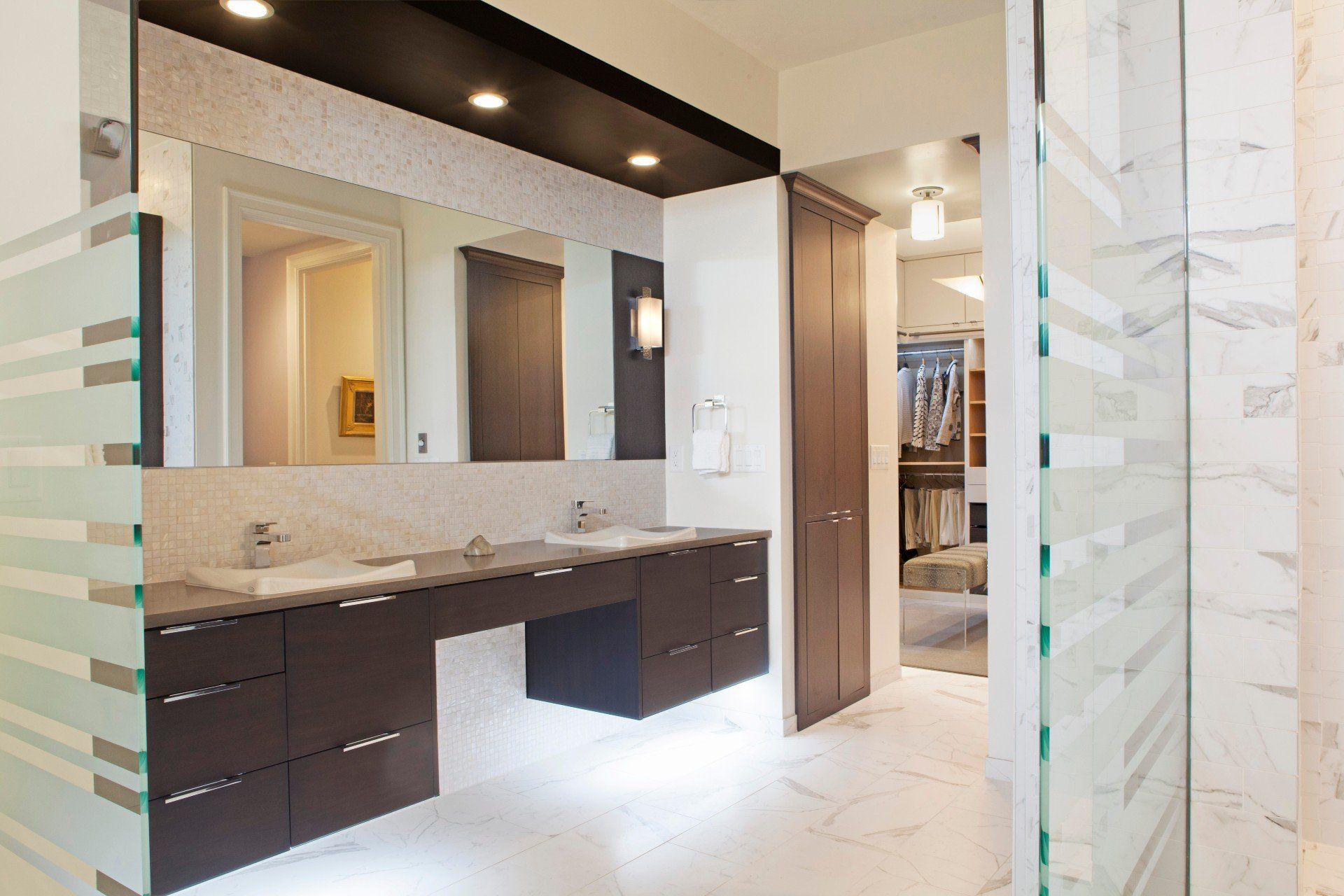 Modern bathroom with dark vanity, large mirror, marble tile, and glass shower enclosure