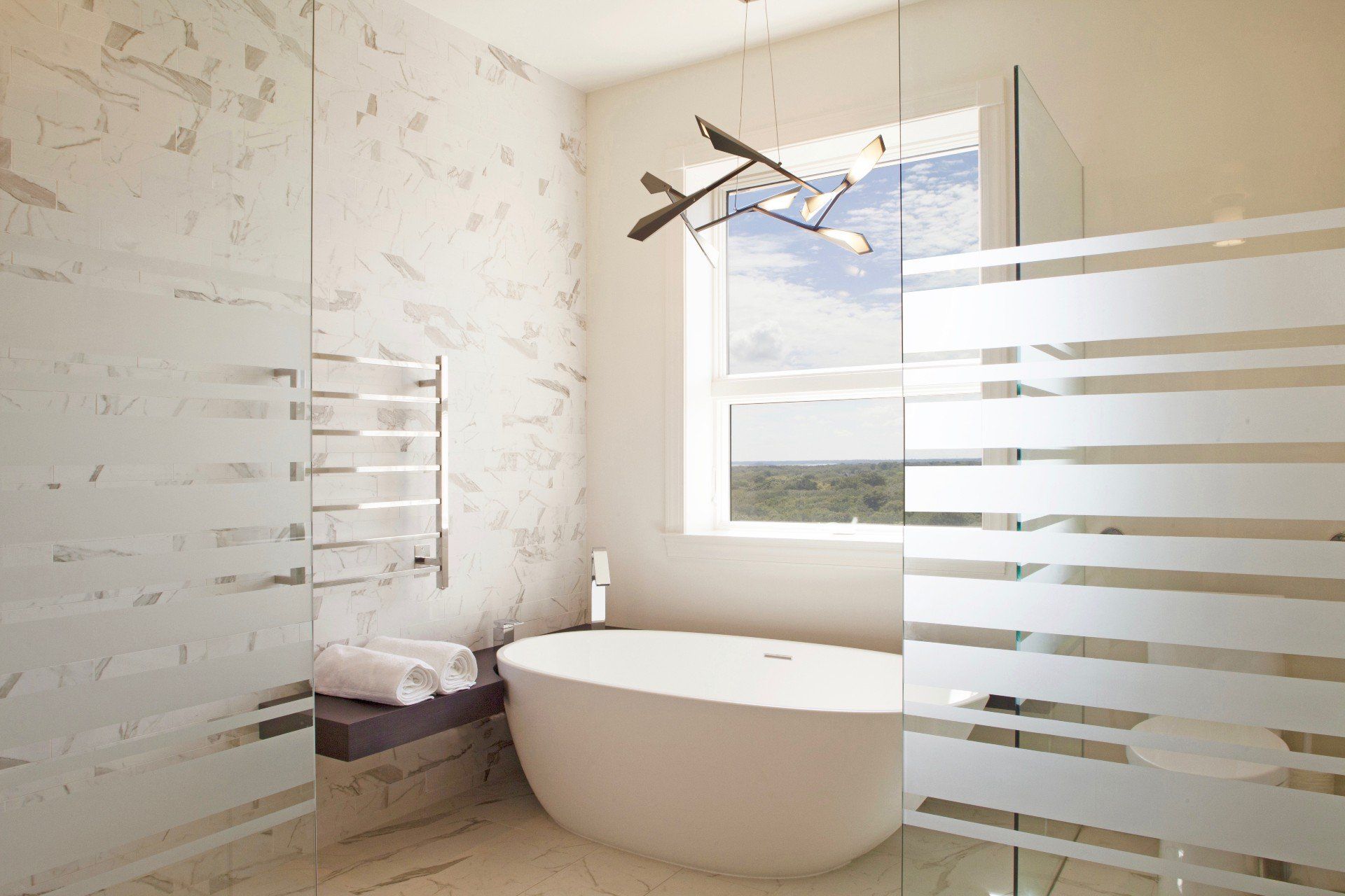 Modern bathroom with a freestanding tub, large window, and frosted glass shower panels