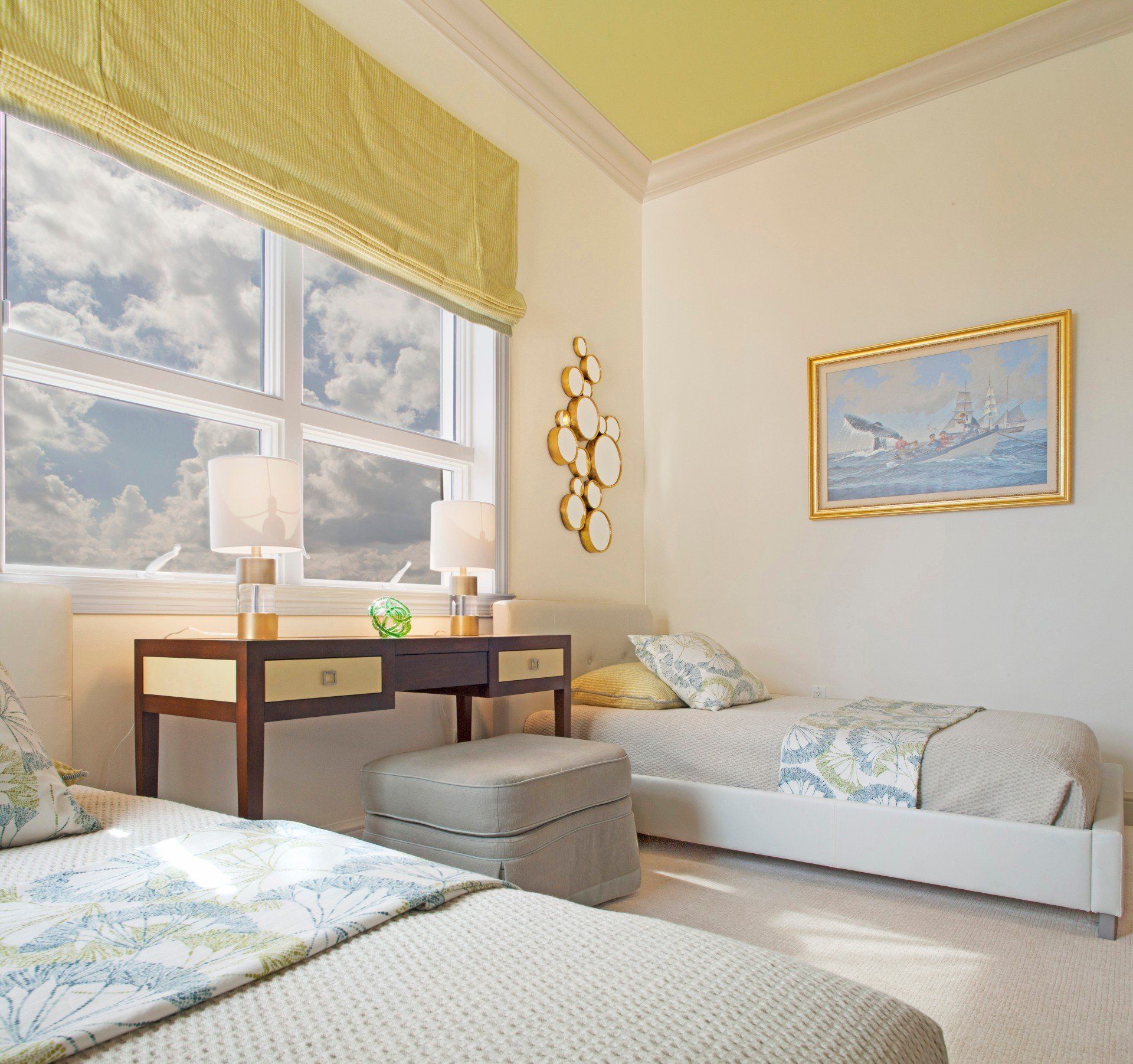 Bright bedroom with two white daybeds, wooden desk by a window, and soft yellow accents