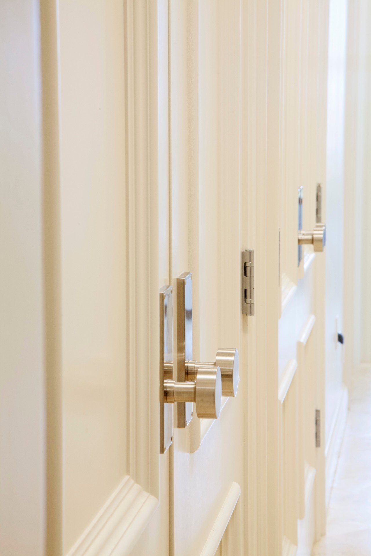 Close-up of white cabinet doors with polished silver handles and trim in a bright interior.