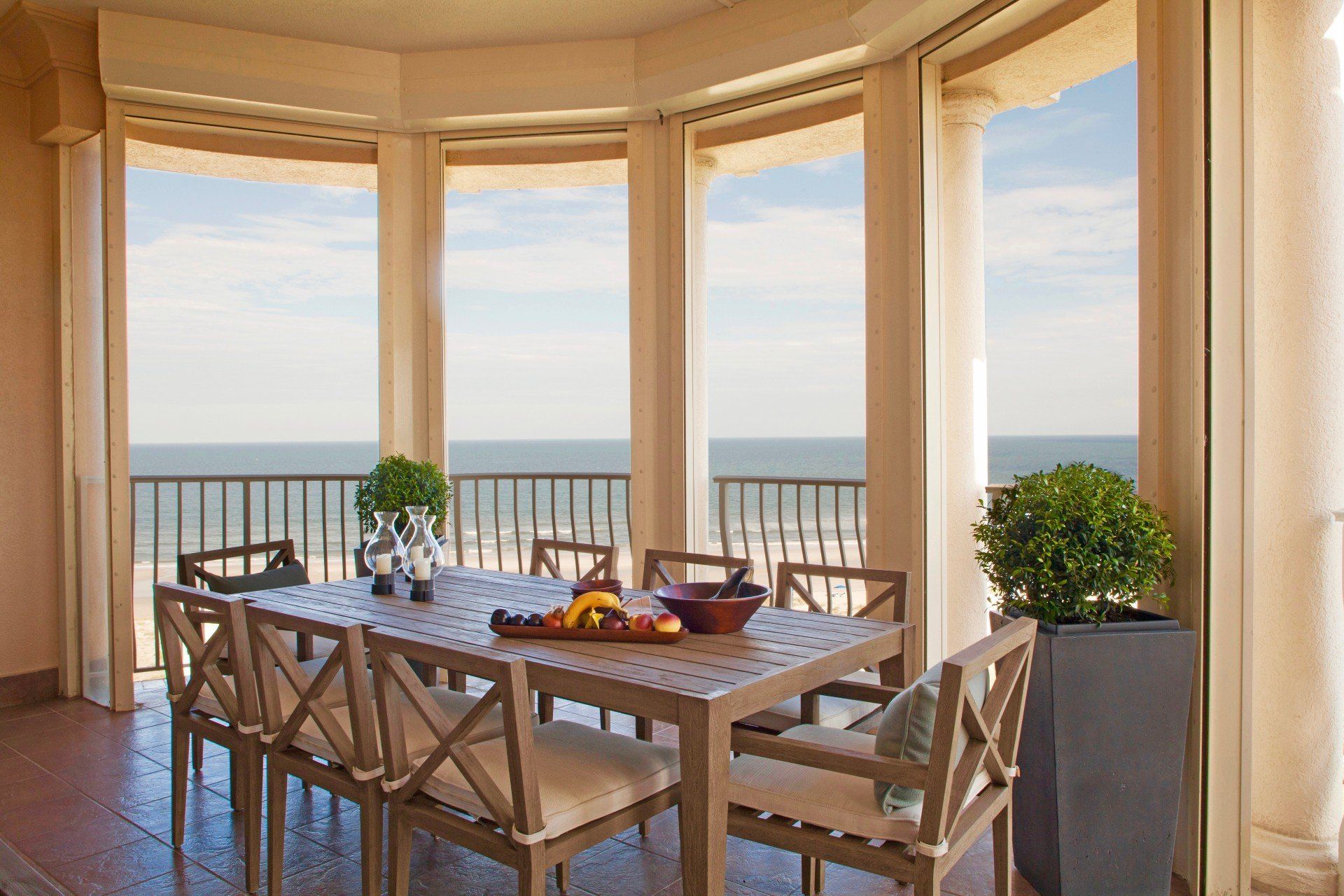 Dining table set on a sunlit balcony with ocean view through large windows
