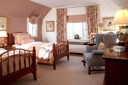 Cozy bedroom with twin wooden beds, pink walls, armchair, and window with floral curtains