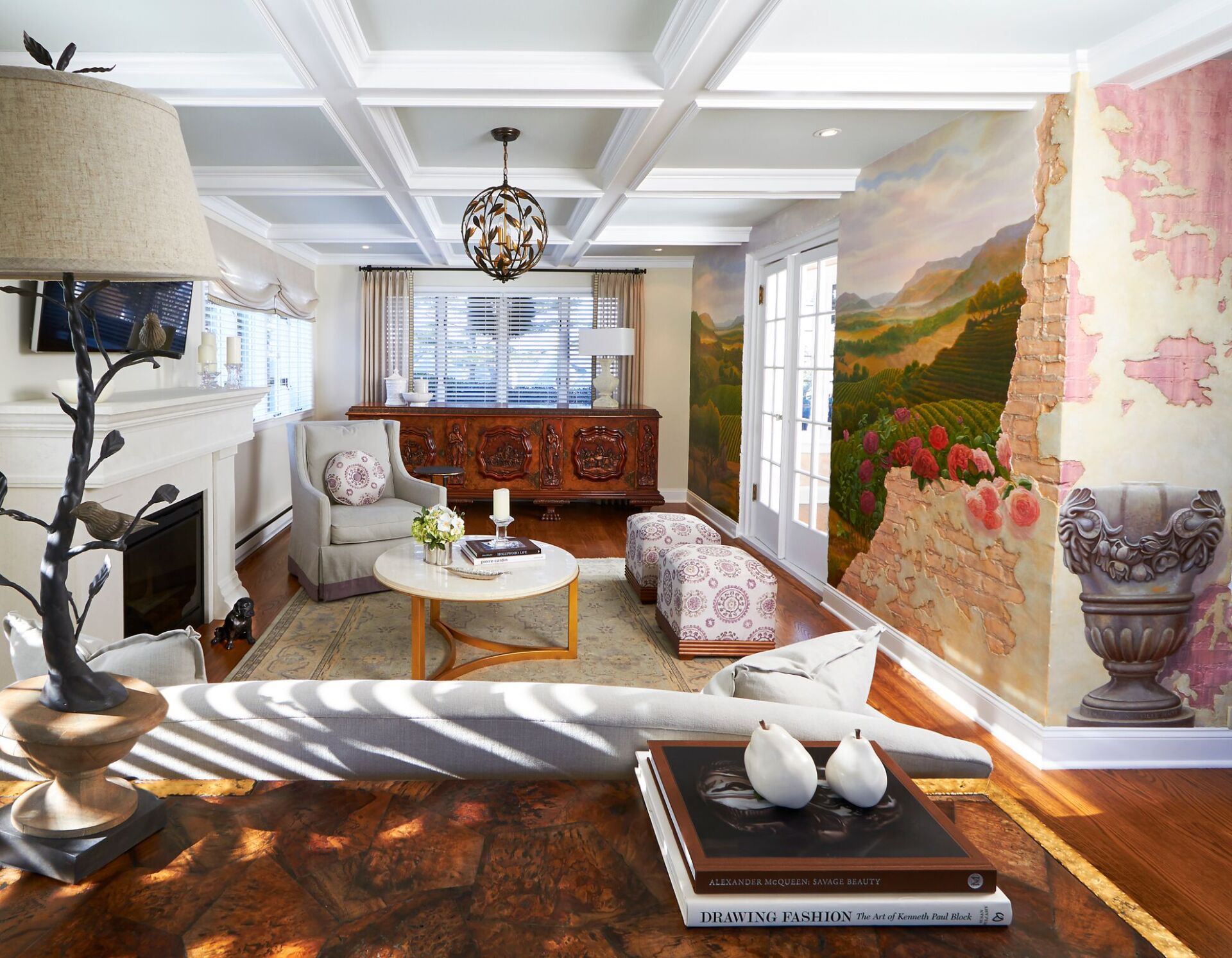 Bright living room with white coffered ceiling, large window, patterned wall art, and wooden furniture
