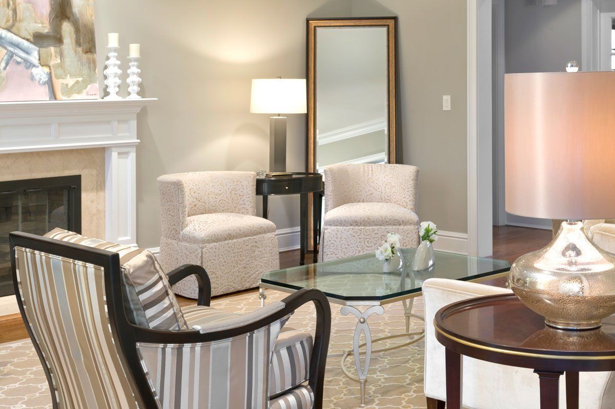 Elegant living room with fireplace, beige chairs, glass coffee table, lamp, and floor mirror