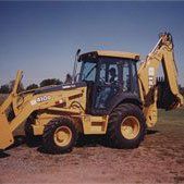 Yellow backhoe on dirt against a blue sky, in a field.