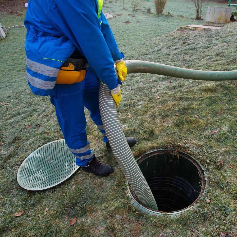 Person in blue overalls pumping a septic tank. Outdoors on grass.