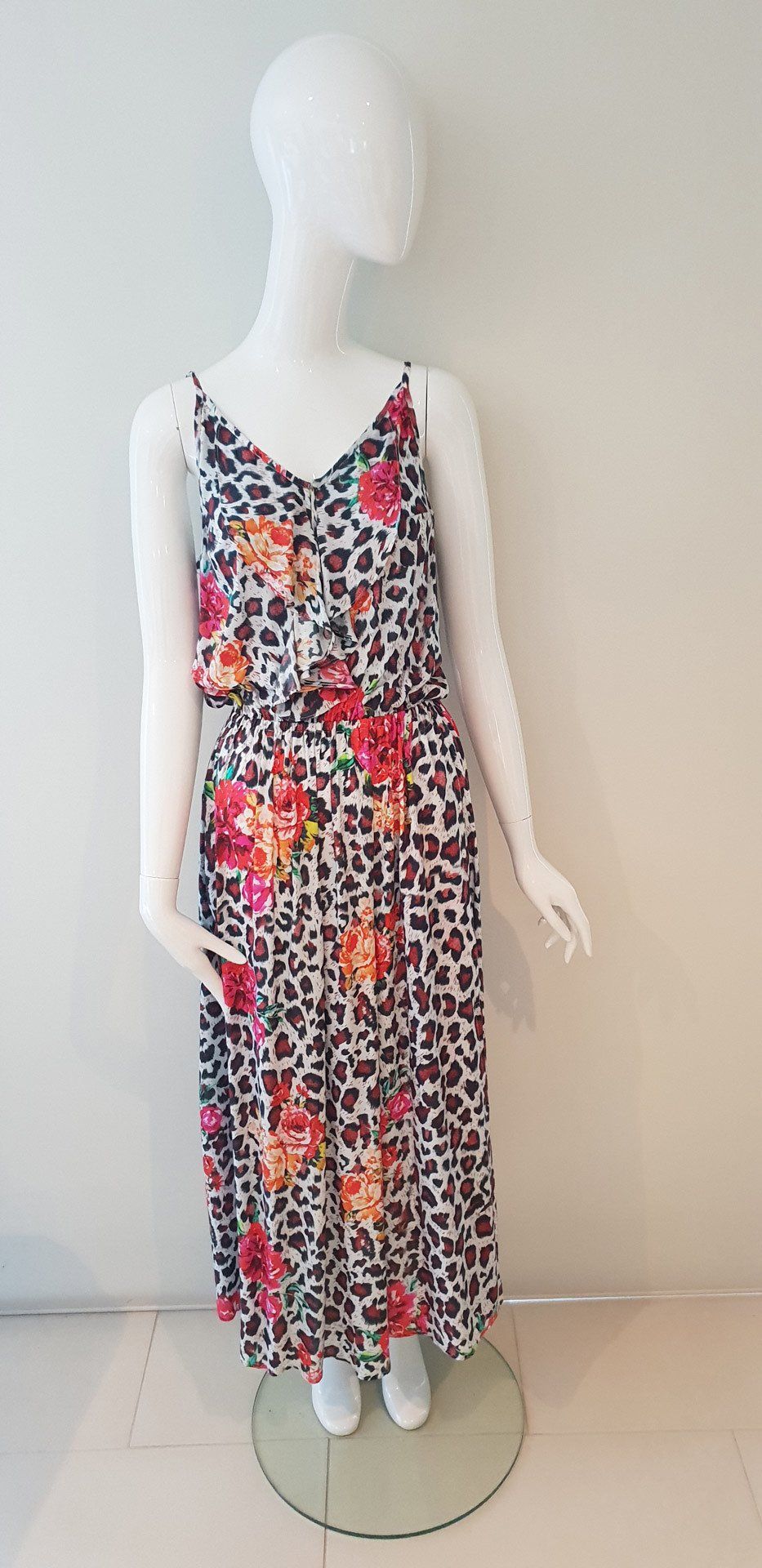 A white mannequin wearing a floral maxi dress stands on a glass circle.