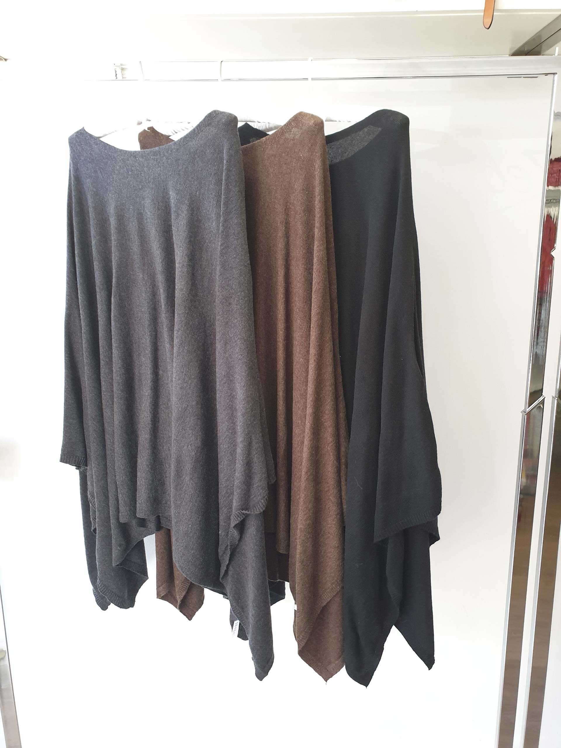 Three long-sleeved tops in gray, brown, and black hanging on a rack against a white backdrop.