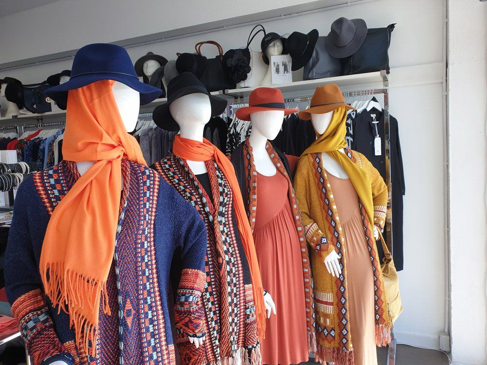 Window display with mannequins wearing hats, scarves, and clothing in warm colors.