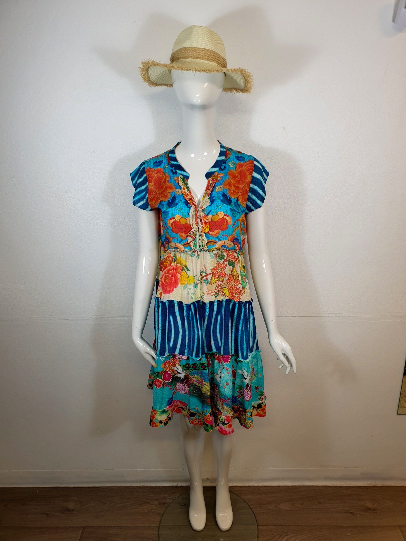 Mannequin wearing a colorful, patterned dress and straw hat. The setting is indoors.