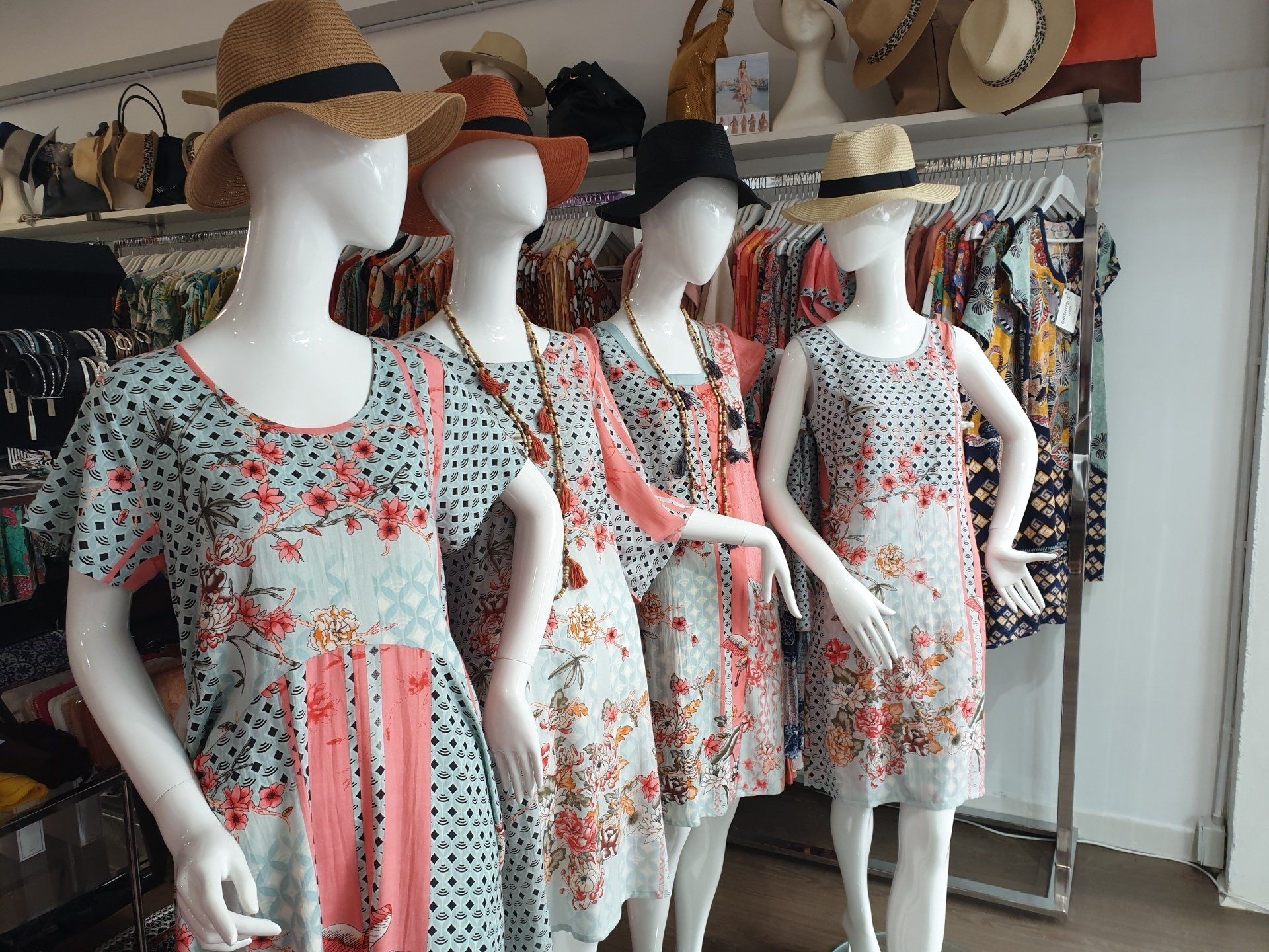 Four mannequins wearing floral dresses and hats in a store.
