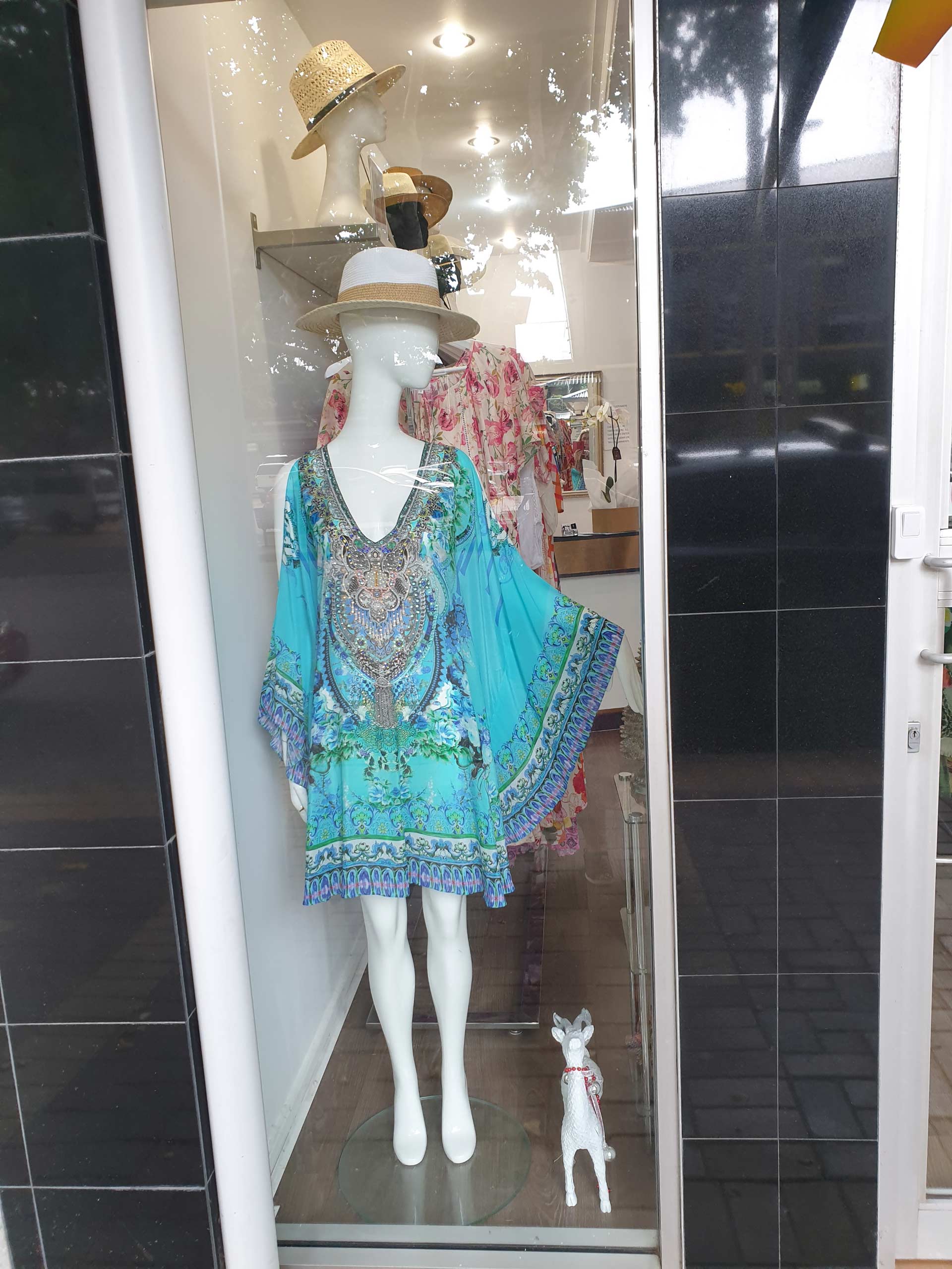 Mannequin in blue dress and hat in shop window with small dog.