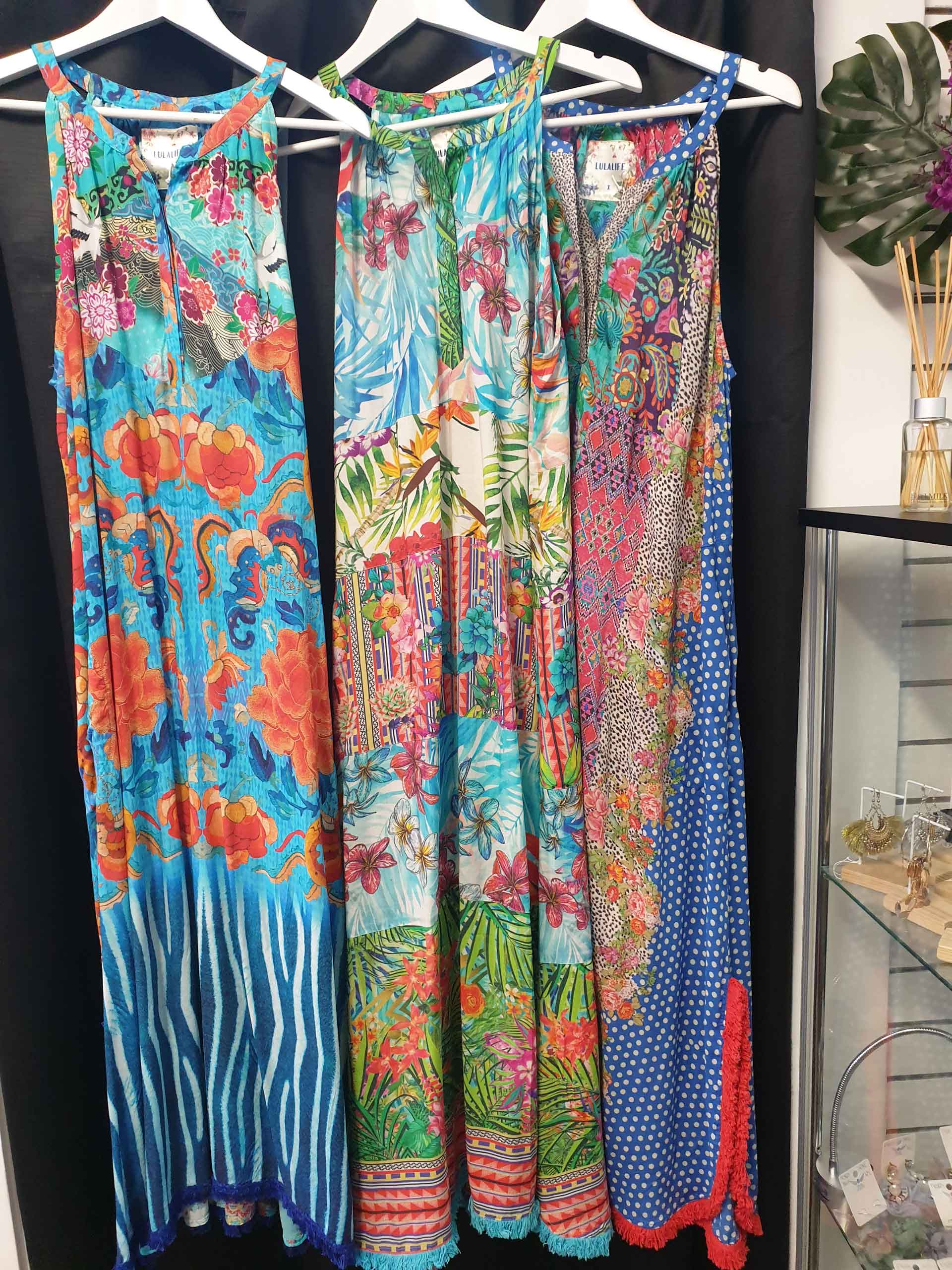 Three colorful floral print dresses hanging on white hangers.