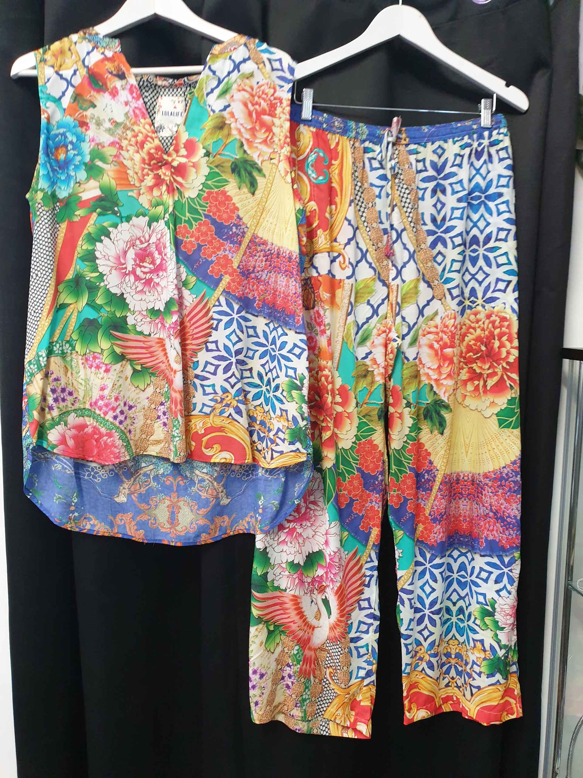 Colorful floral print top and pants set hanging on white hangers.