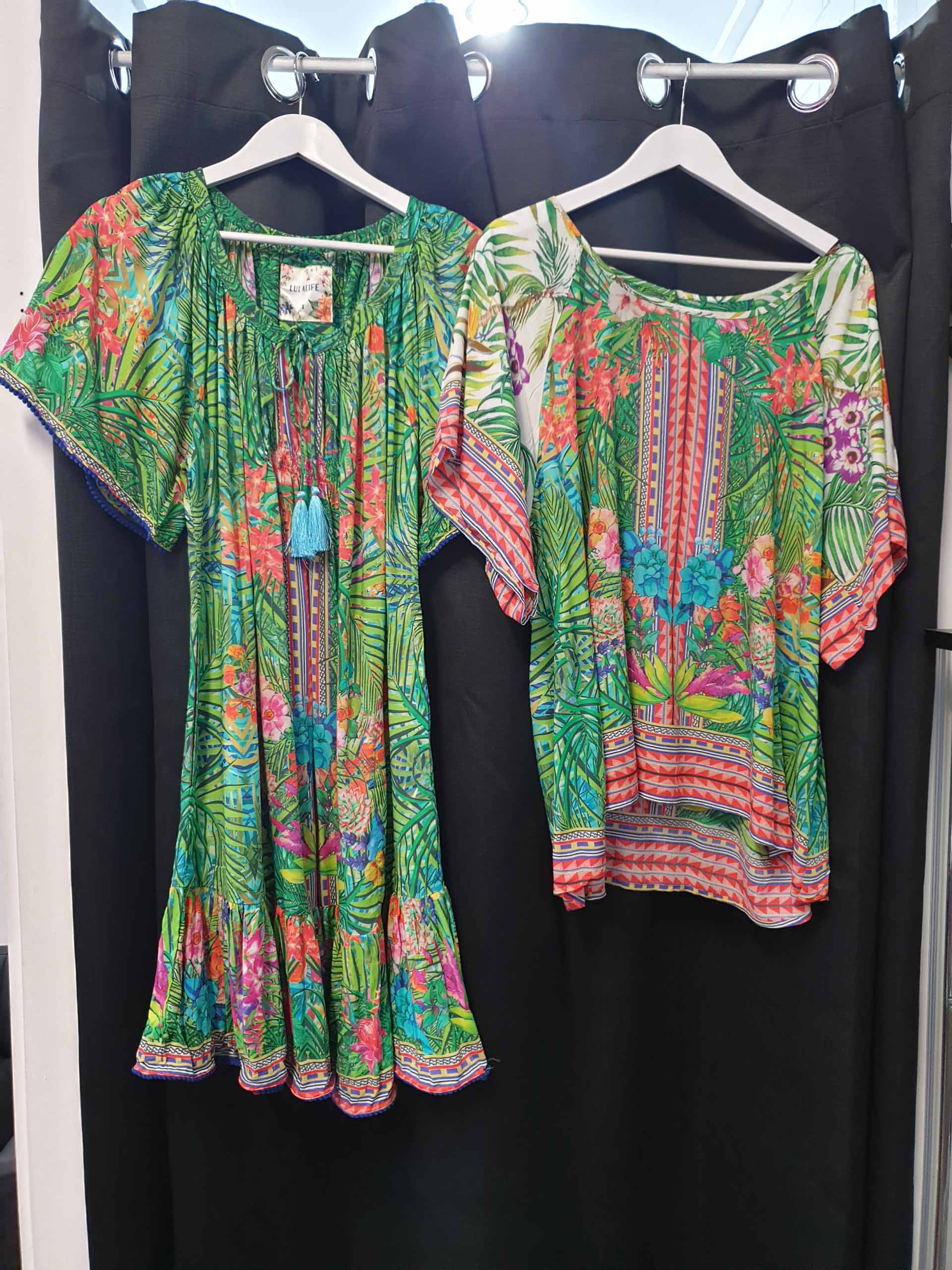 Two colorful floral print dresses hanging on hangers in a shop.