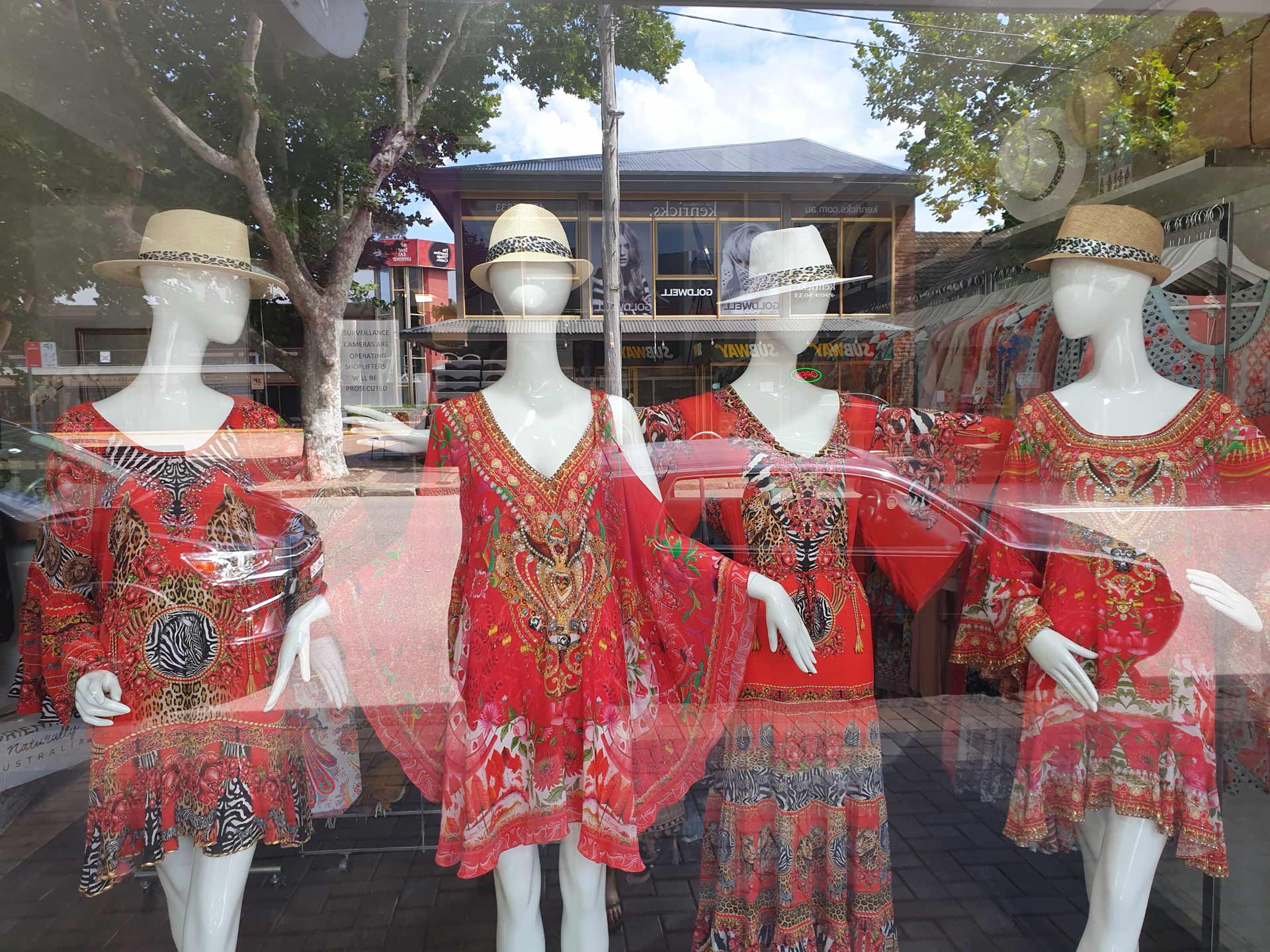 Window display with mannequins wearing red patterned dresses and hats.