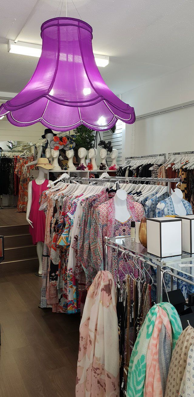 Inside a clothing store, clothing racks, mannequins, and a large purple lampshade.