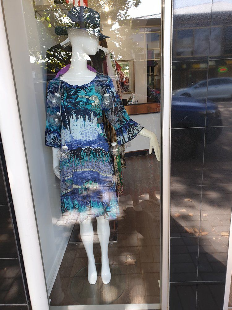 Mannequin in a shop window wearing a blue patterned dress and hat.