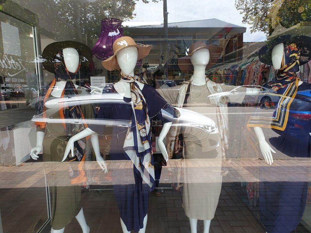 Mannequins in a storefront window display; hats, scarves, and clothing.
