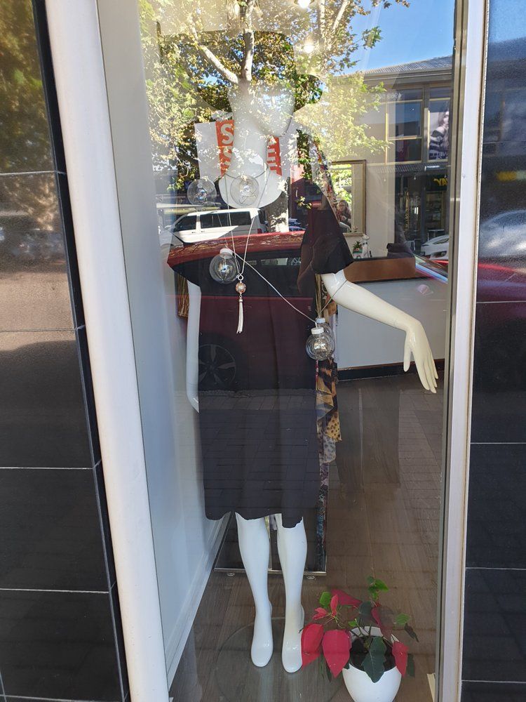 Mannequin in a shop window, wearing a dark dress, jewelry, and a black head covering.