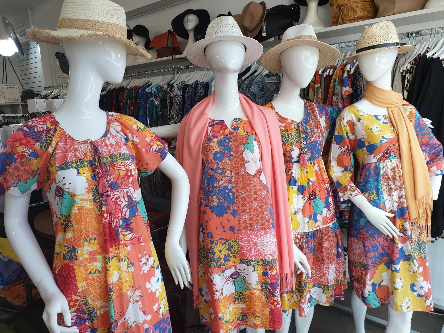 Four mannequins in a clothing store wearing colorful floral dresses and straw hats.