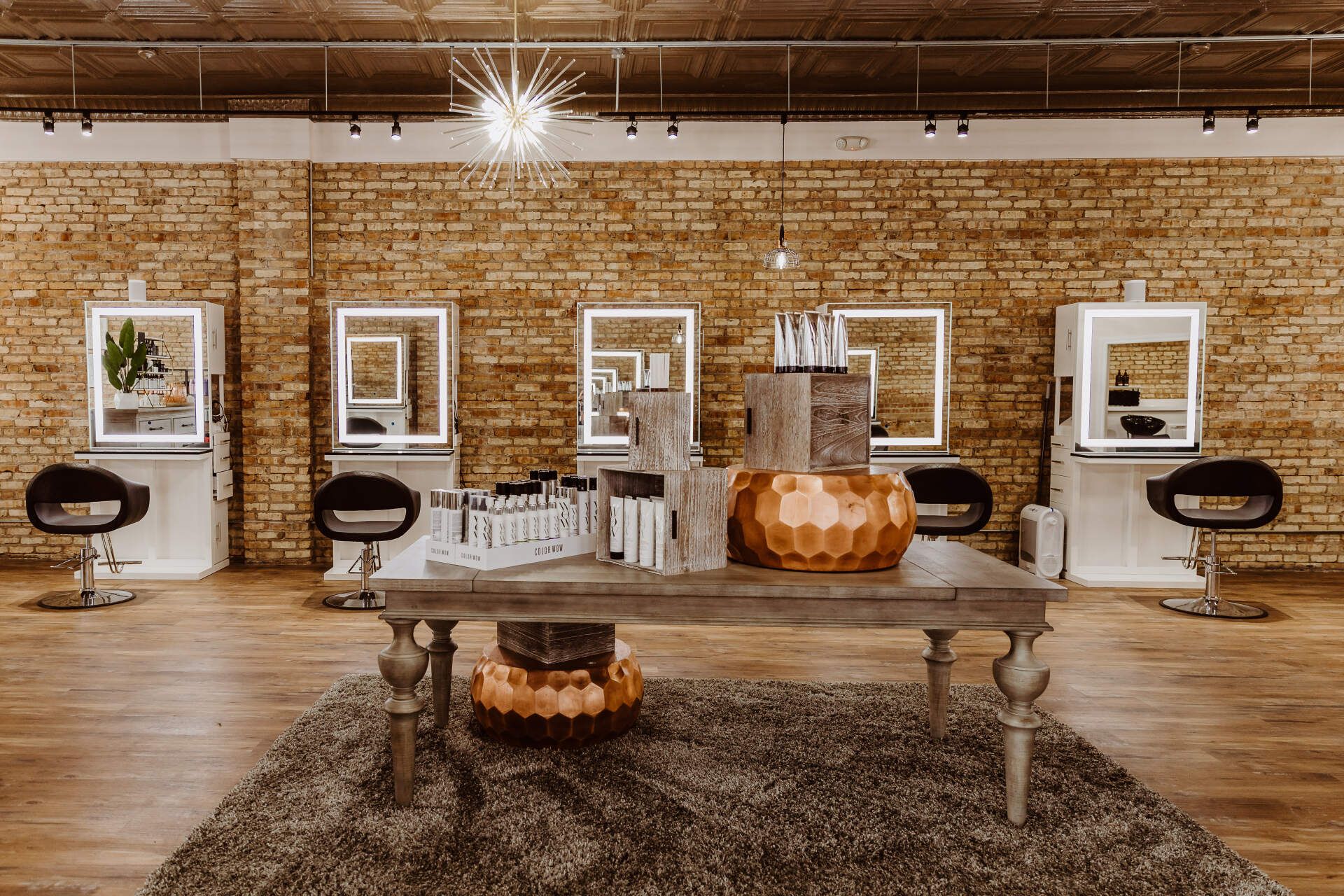 Hair salon interior with brick wall, illuminated mirrors, chairs, and product display.