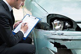 A man with a clipboard, assessing accident damage on a car
