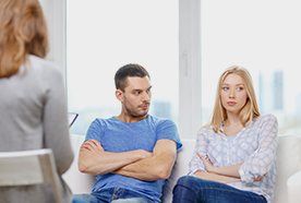 A man sitting with folded arms, glaring at the lady next to him, as they sit opposite a female solicitor
