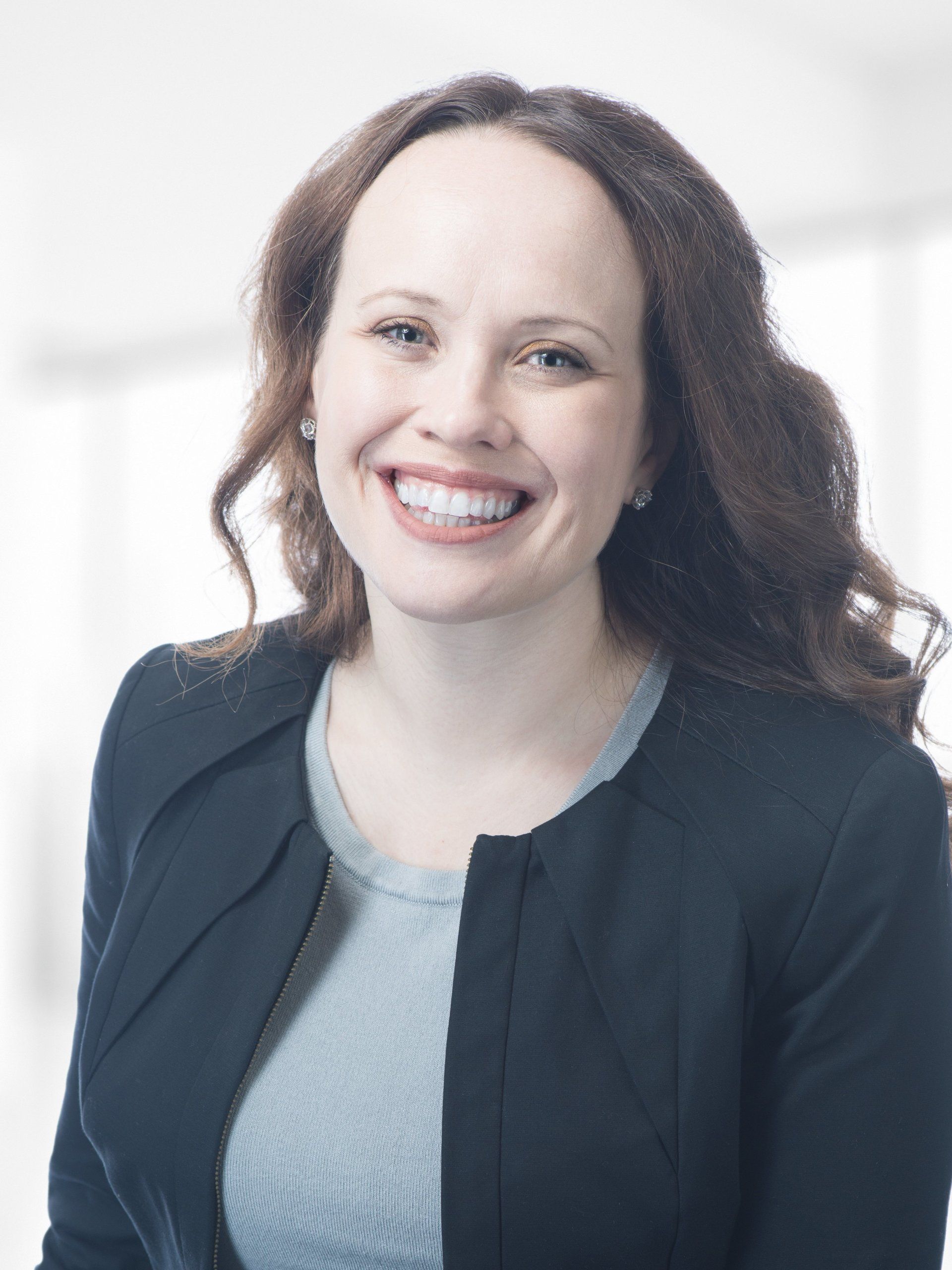 A woman in a black jacket and gray shirt is smiling for the camera.
