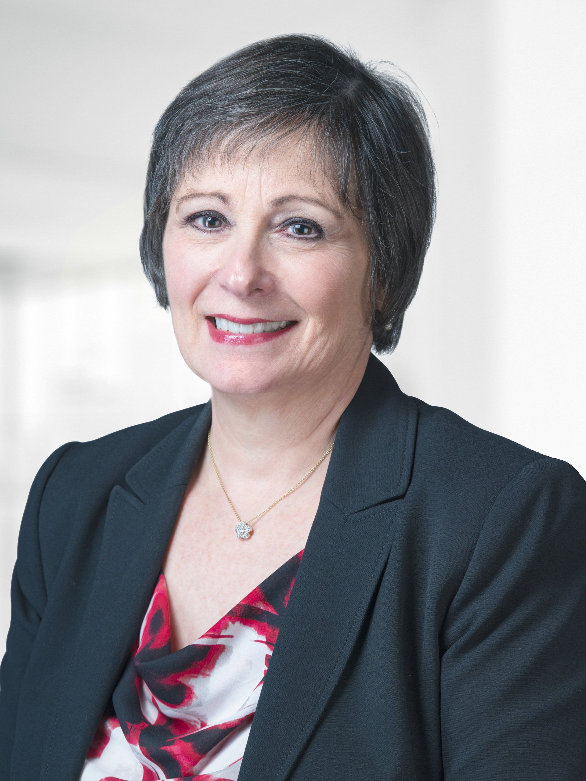 A woman wearing a black jacket and a necklace is smiling for the camera.