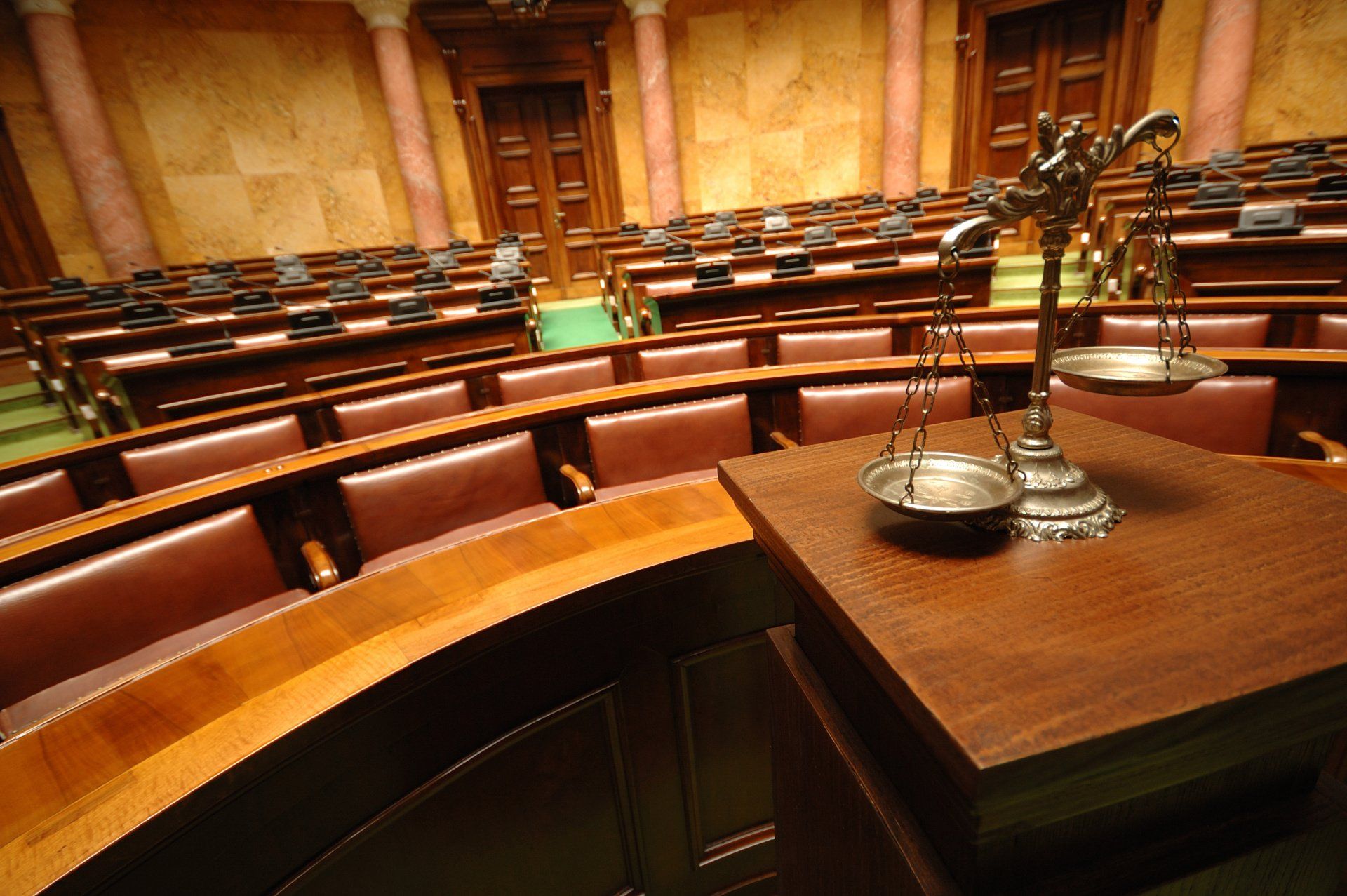 A scale of justice sits on a wooden table in a courtroom