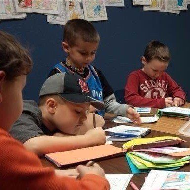 A group of children are sitting at a table writing in notebooks.