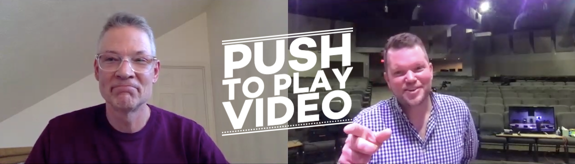 Two men are sitting in front of a sign that says push to play video
