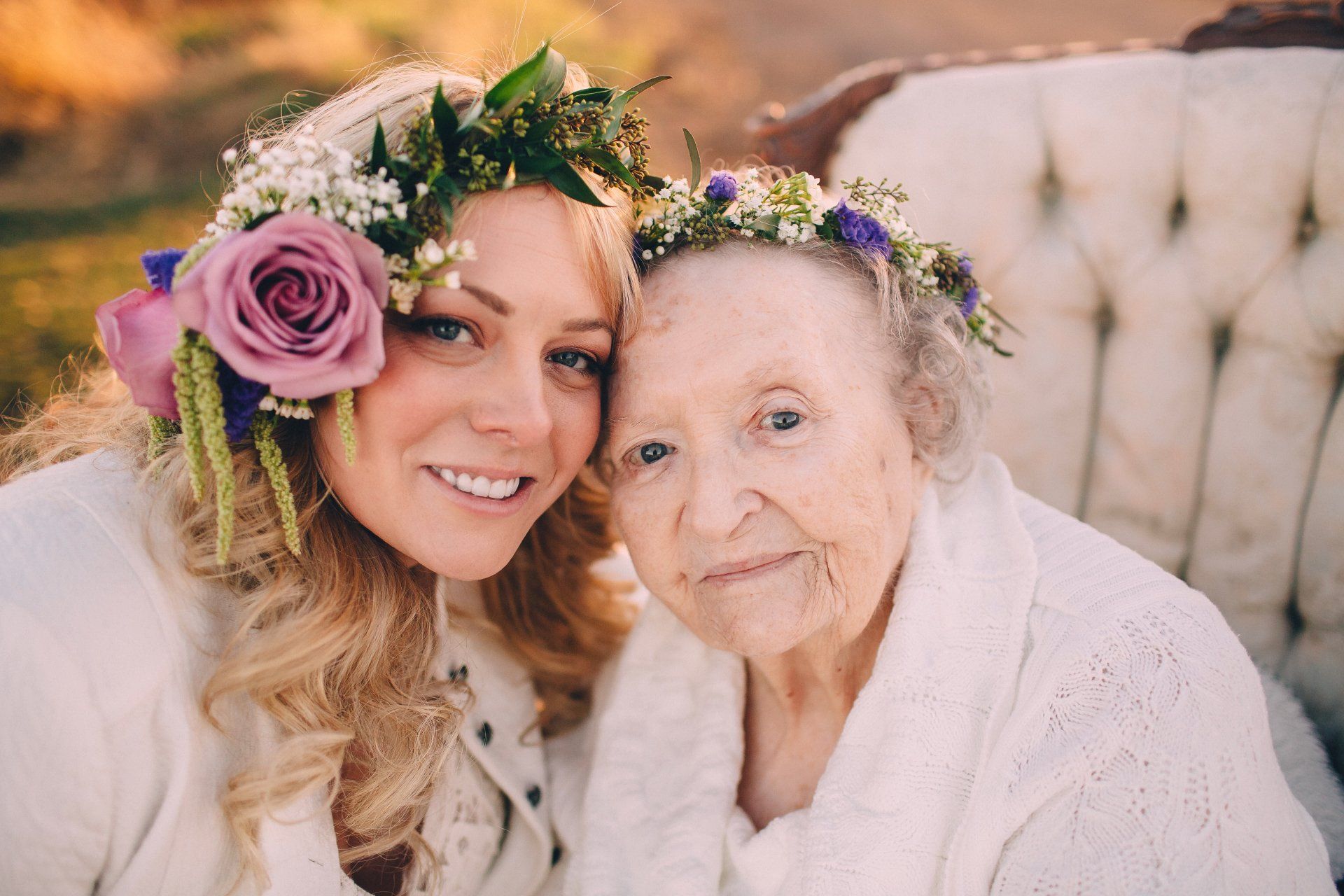 Woman and older person with floral crowns smiling, outdoors.