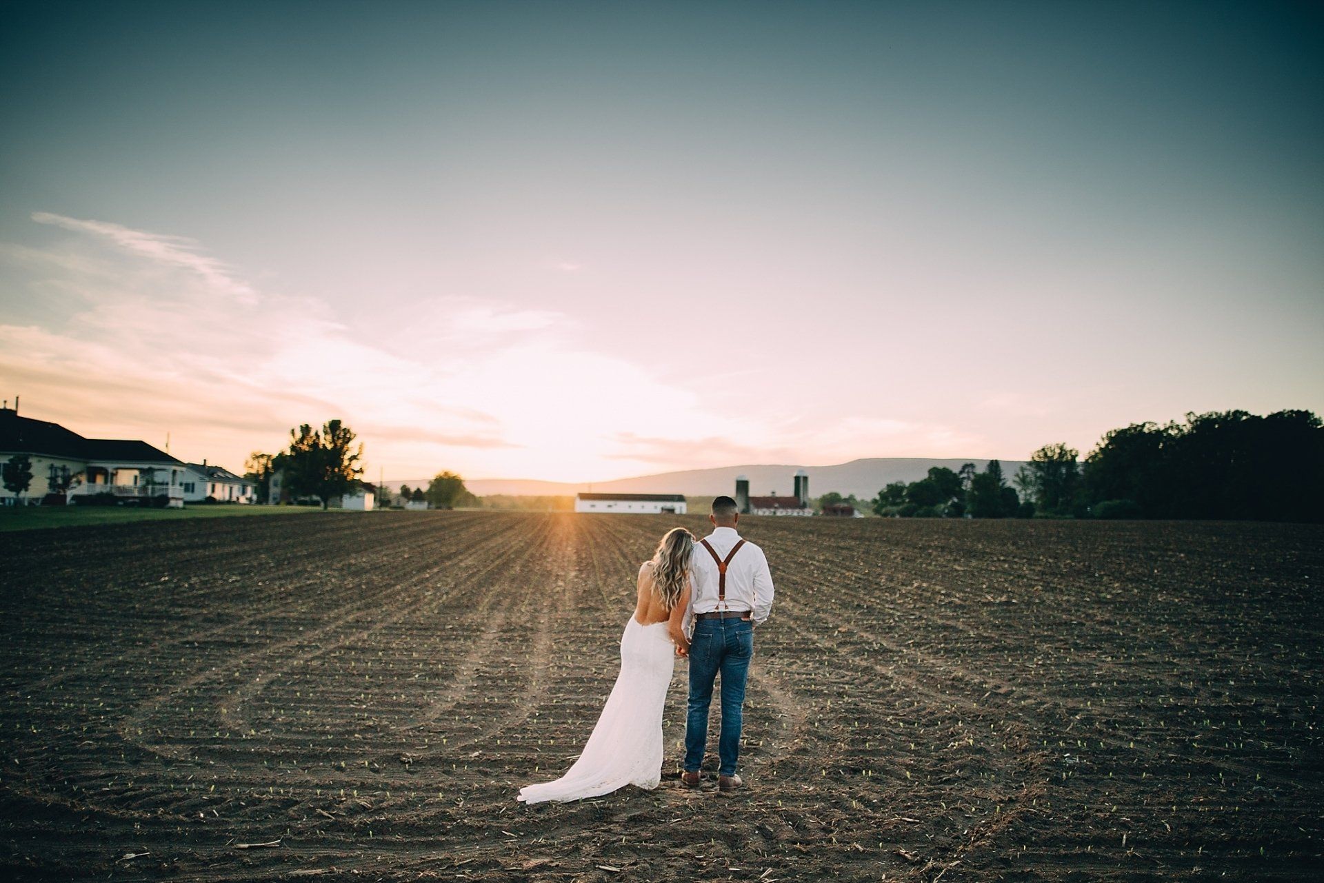 Couple walking in a field at sunset, man with suspenders, woman in wedding dress.