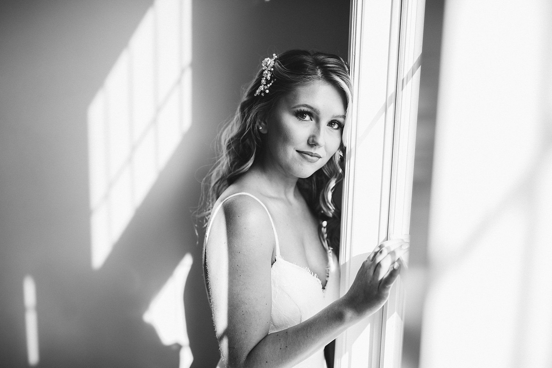 Woman in white dress leans against a window; light and shadows play across her face.
