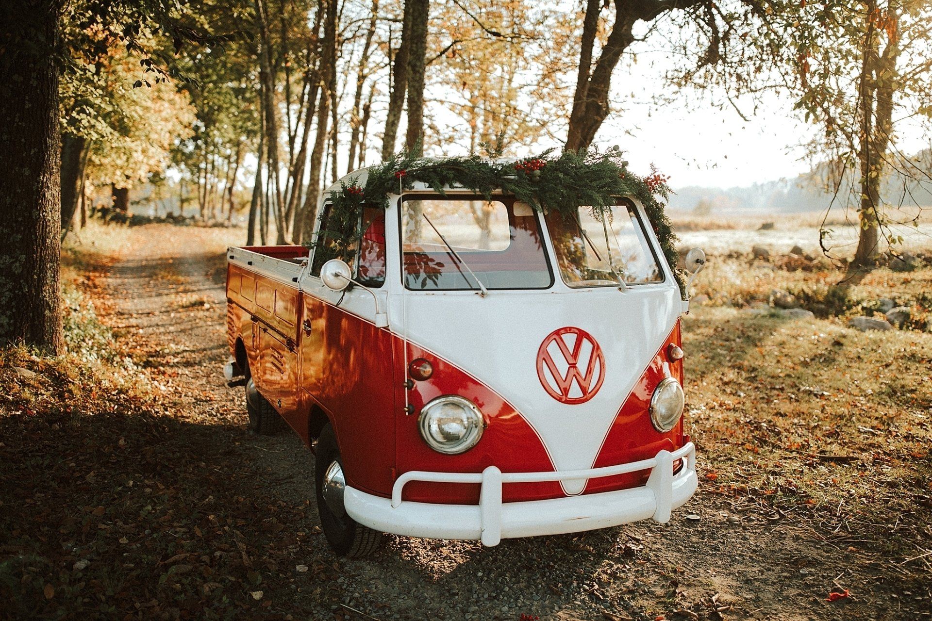 Red and white Volkswagen bus with wreath, parked on a path in a wooded area.