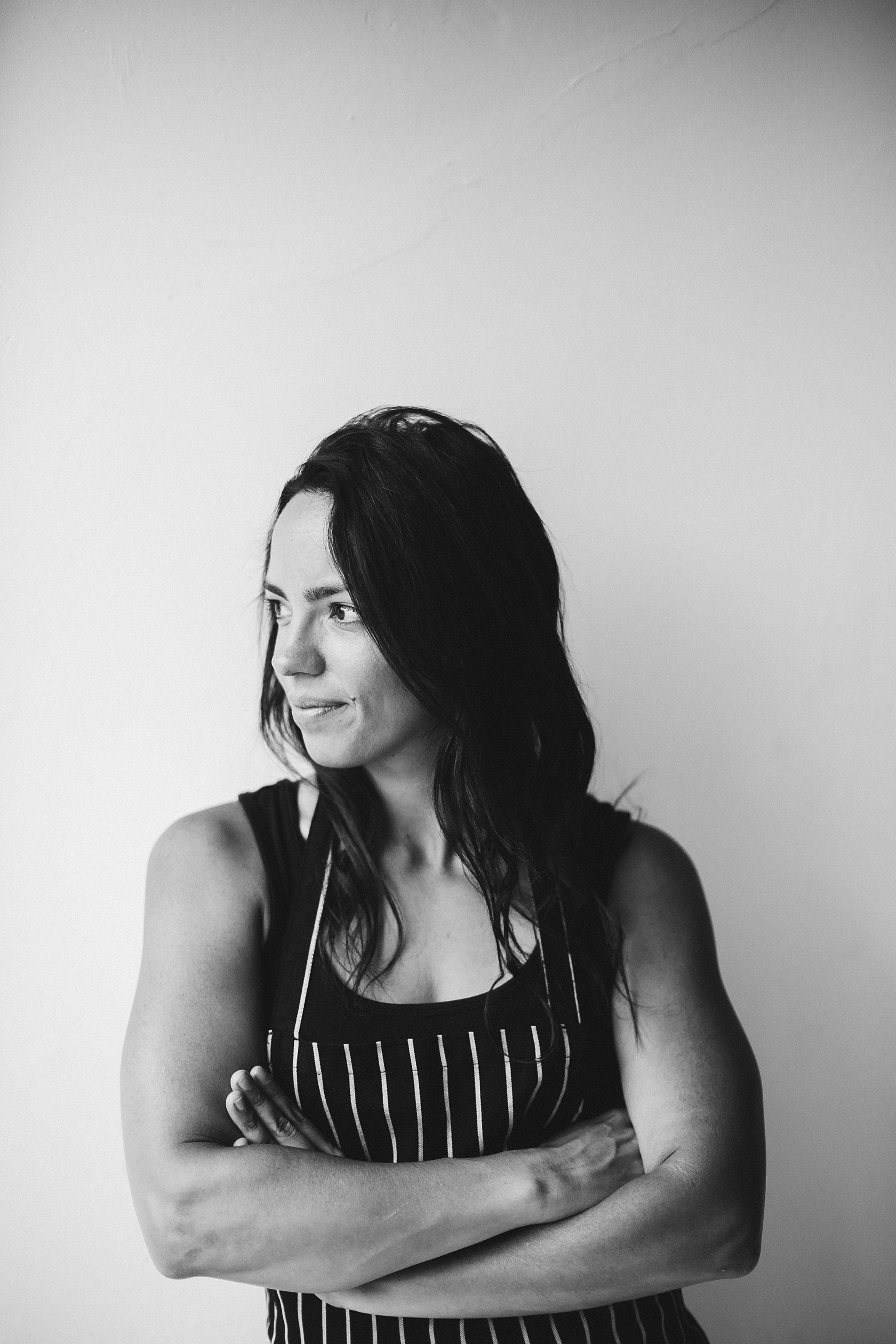 Woman with crossed arms, wearing a striped apron, looking off to the side.