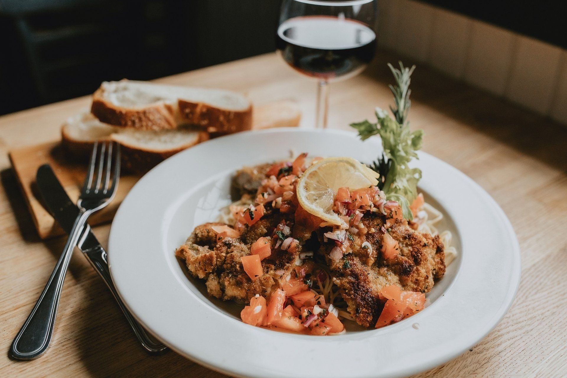Plate of food with bread, wine glass, and silverware on a table.