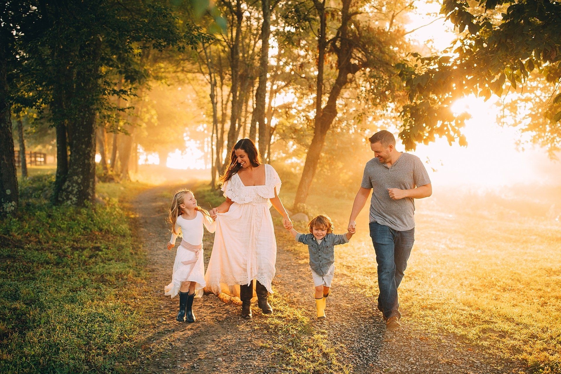 Family of four walking hand-in-hand down a path in a sunlit forest.