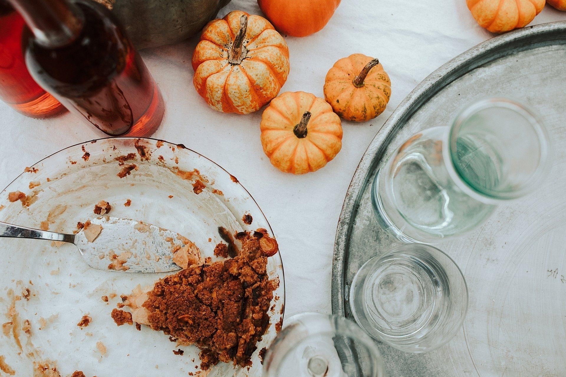 Table with mini pumpkins, a partly eaten pie, glasses, and a bottle of red liquid.