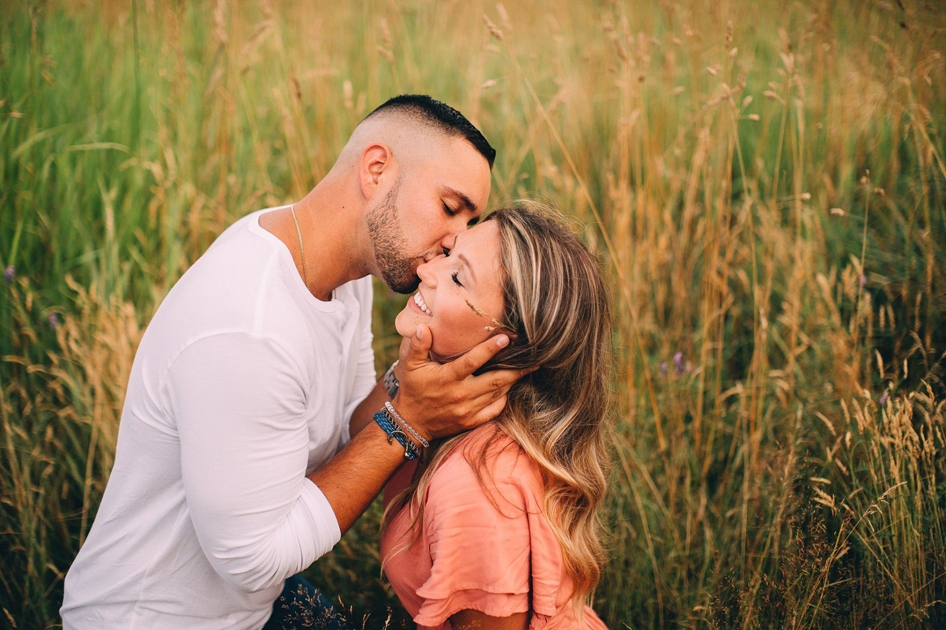Man kisses woman's forehead in field of tall grass. Both smiling, man holding her face. Hudson Valley