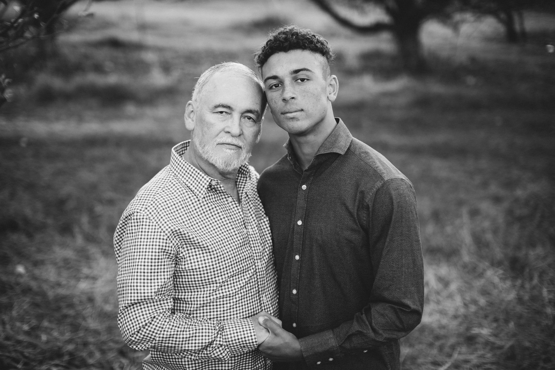 Two men standing close, holding hands; outdoors, black and white.