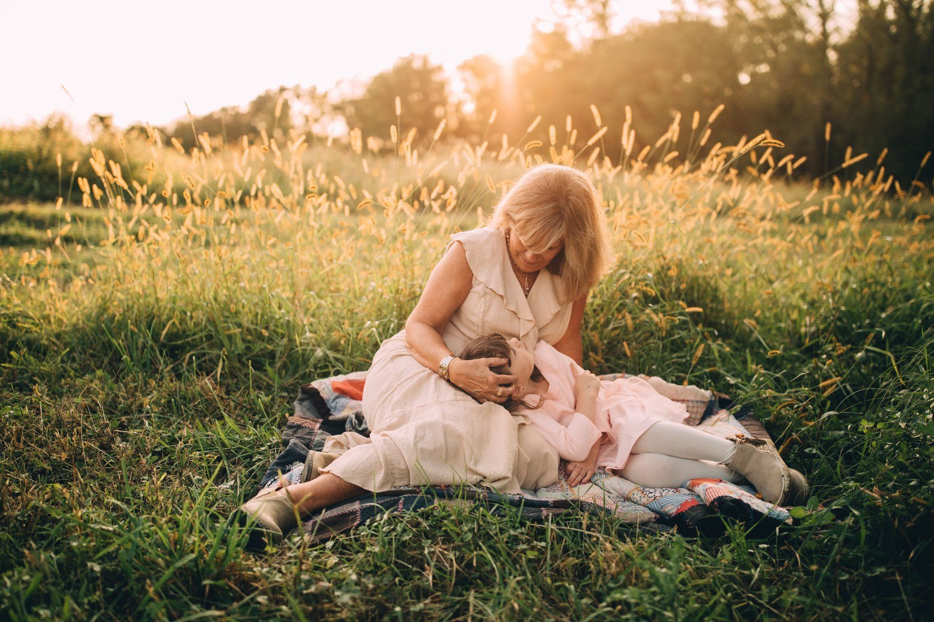 Woman and child on a blanket in a grassy field; sunlight streams through the background.