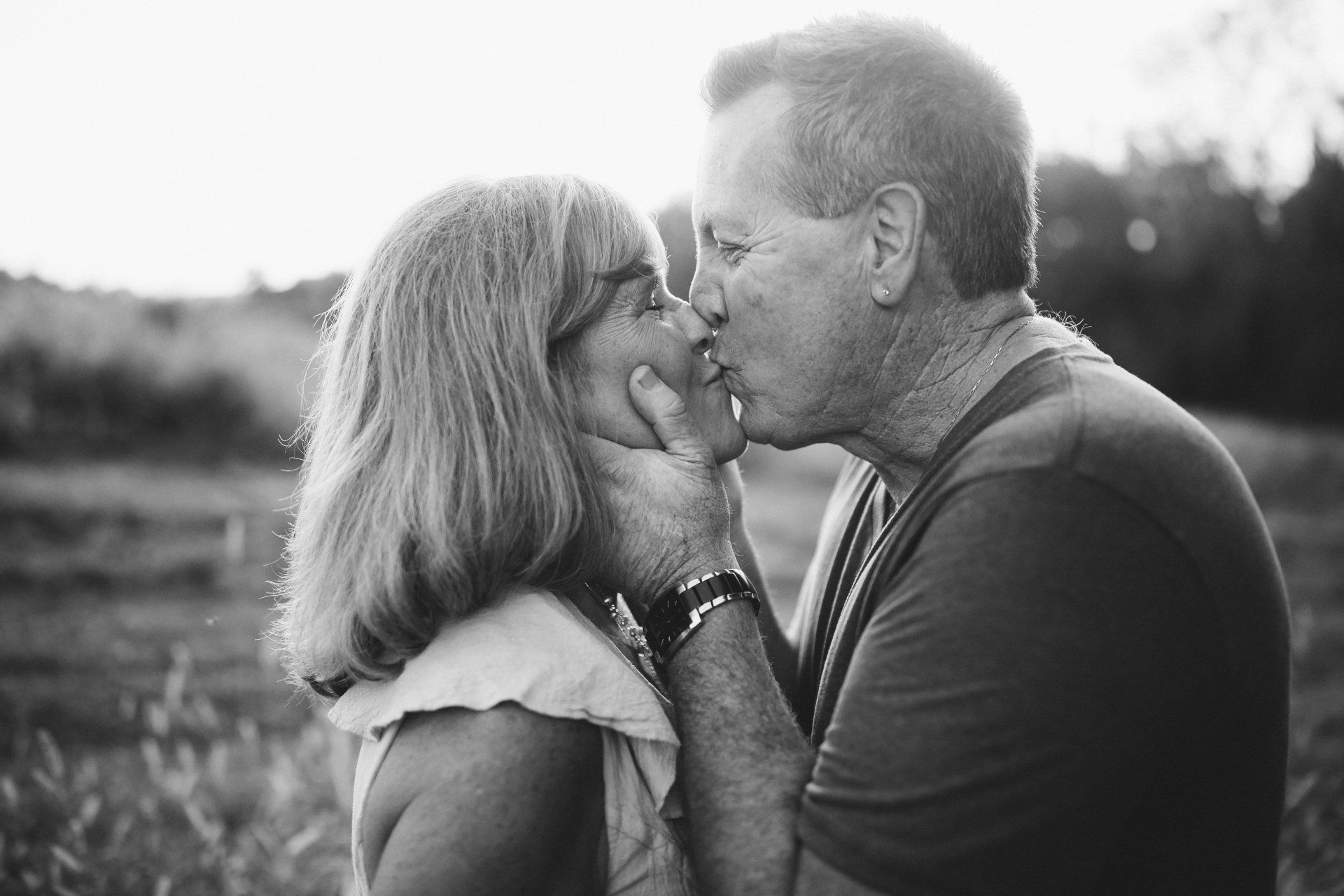 Couple kissing outdoors, man holding woman's face, backlit by the sun. Black and white.