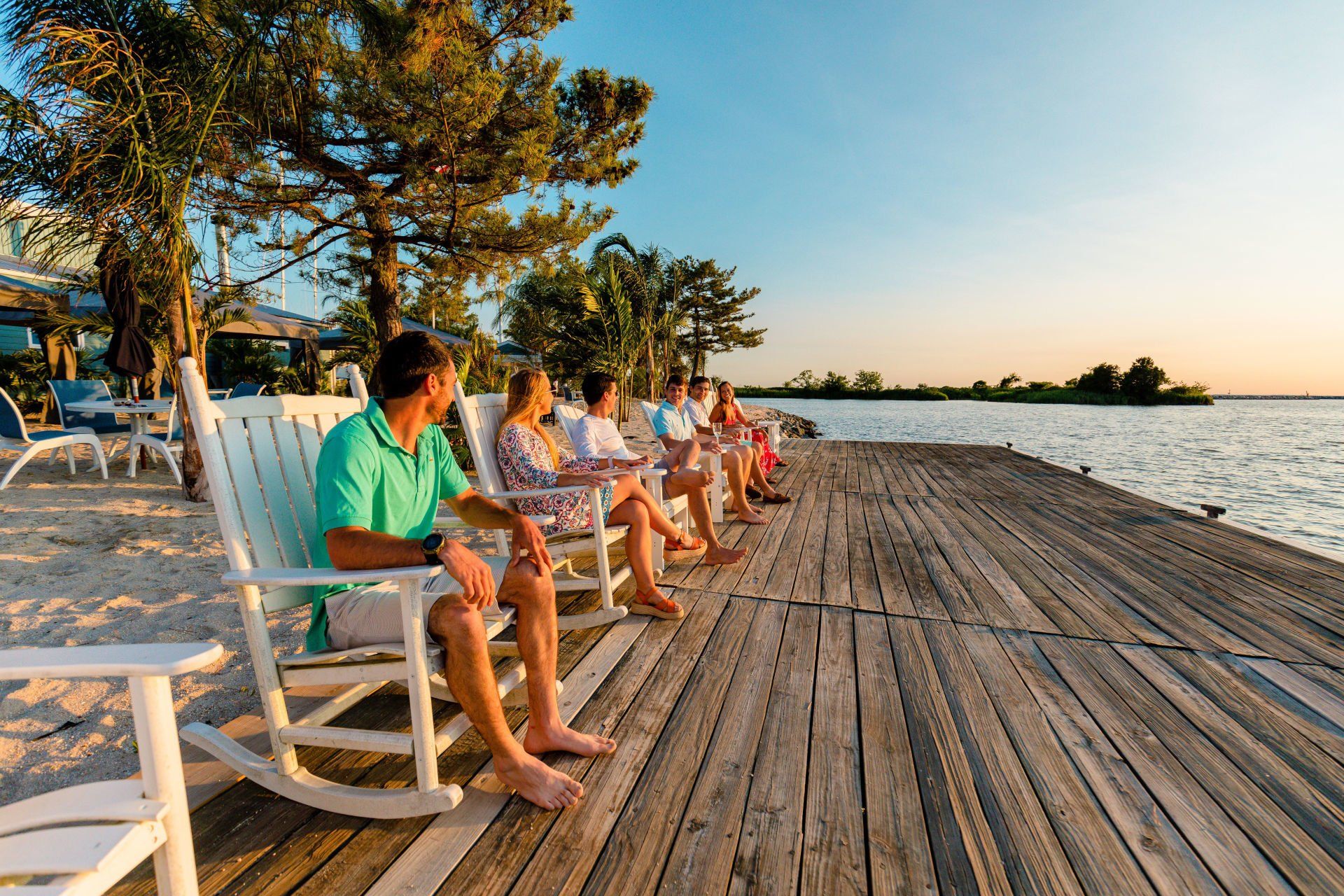 Group of people sitting in chairs on a deck watching the sunset