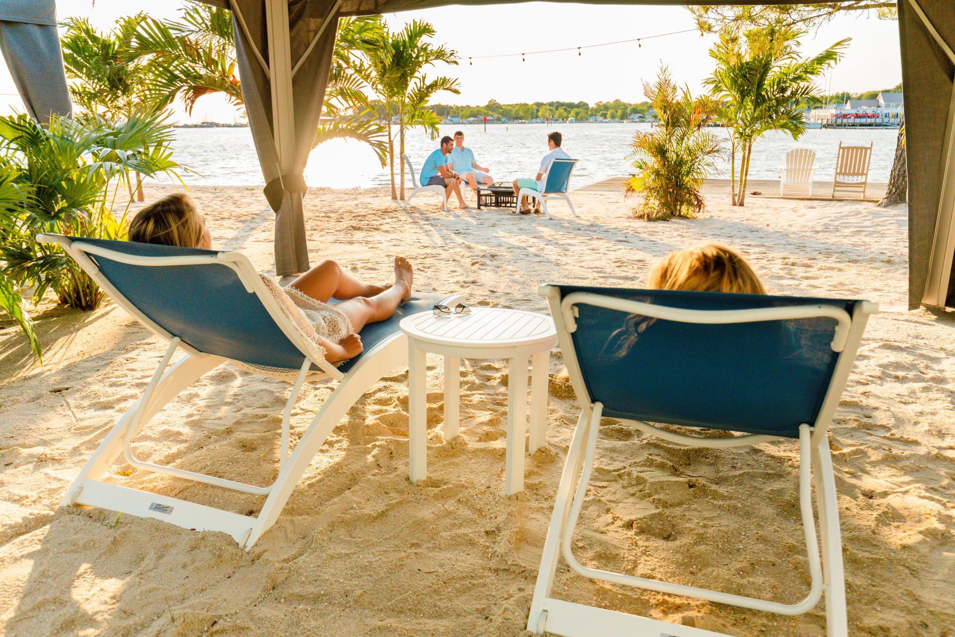Two women on beach laying in chairs under a cabana