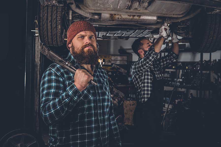 A man with a beard is holding a wrench in a garage.