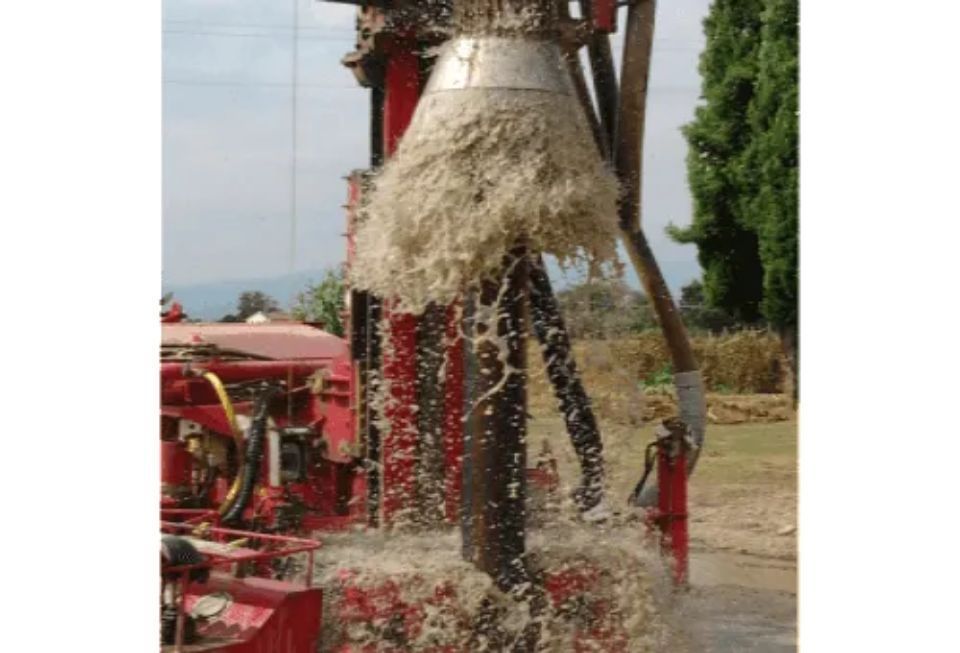 Una piattaforma di perforazione espelle materiale schiumoso e di colore chiaro; una macchina rossa in un ambiente esterno.