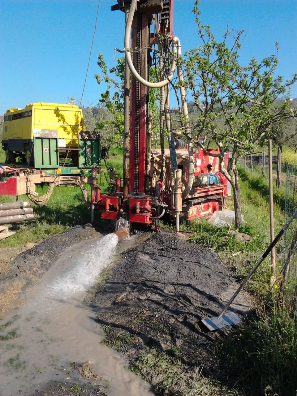 Piattaforma di perforazione in una zona erbosa, spruzzi d'acqua, cumulo di terreno scuro.